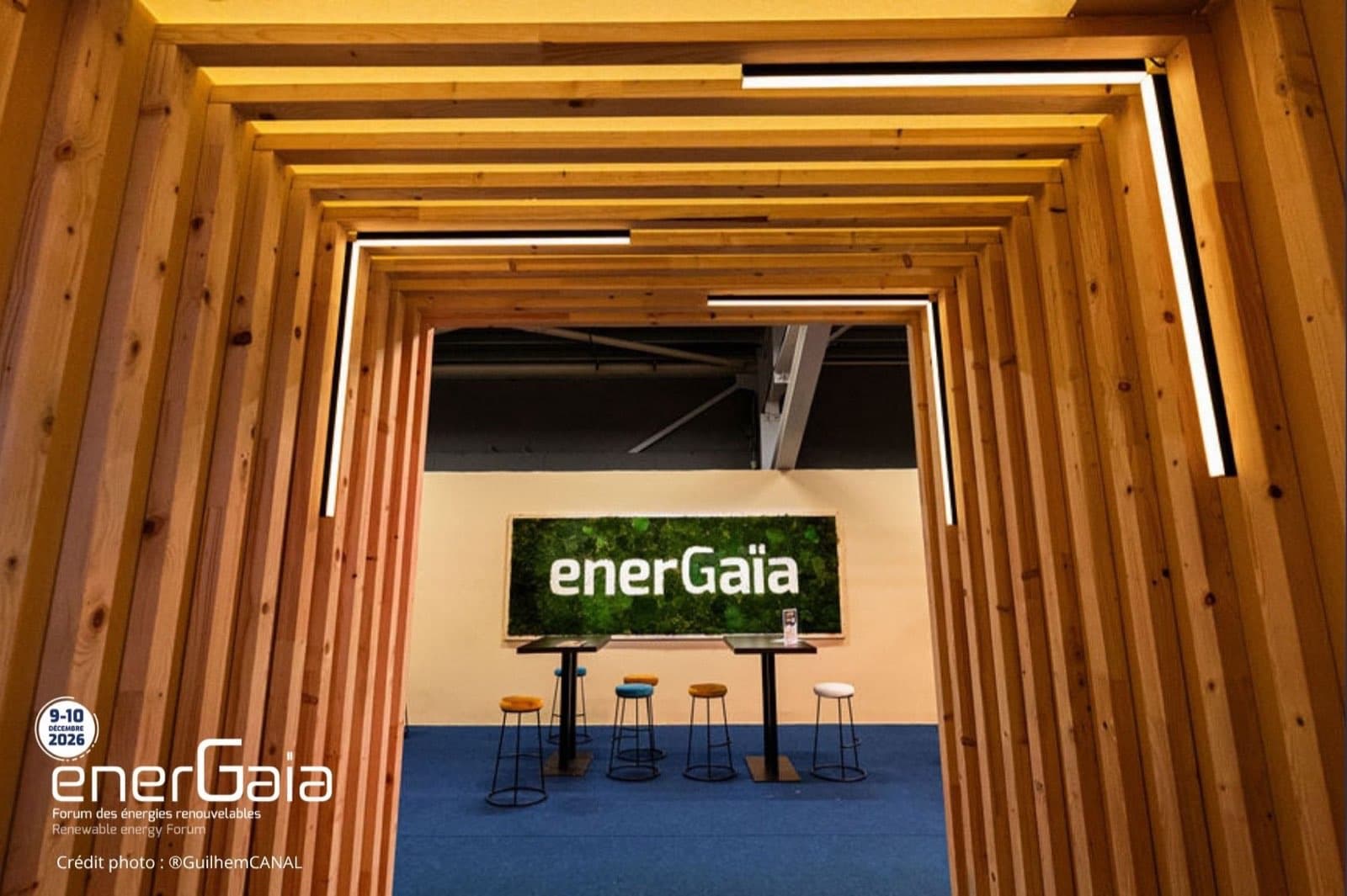Espace de rencontre en bois du Forum EnerGaïa, avec le mur végétal au logo du salon